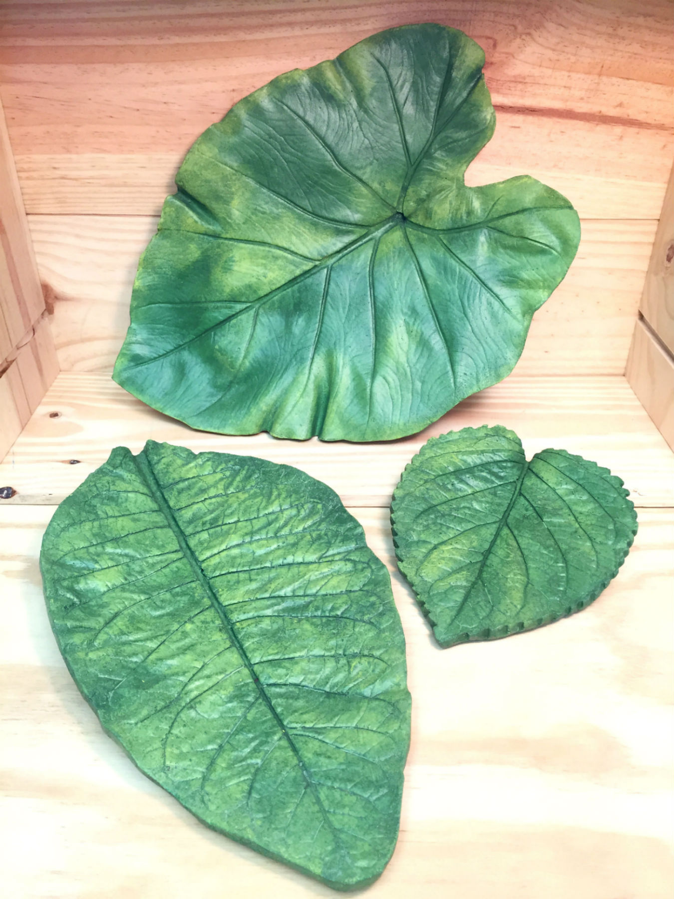Three leaf plates that are painted green and vary in size from small to large